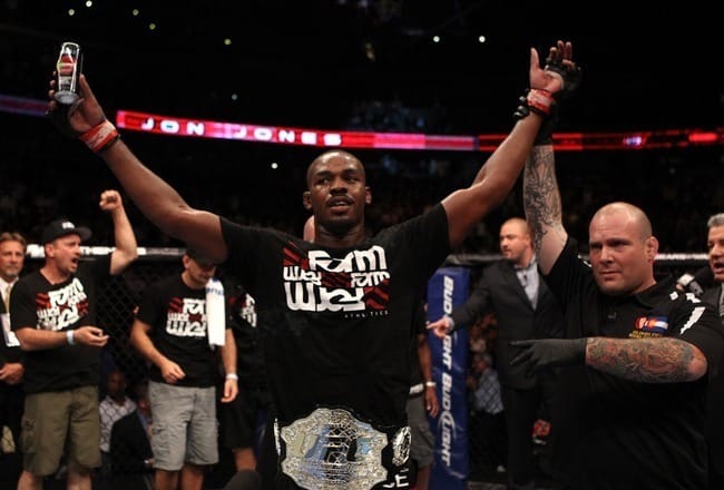 Jon Jones raises his arm in celebration with the UFC light heavyweight belt around his waist inside the Octagon