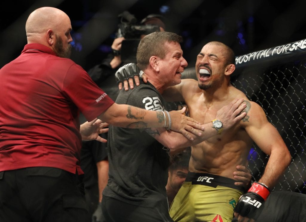 Jose Aldo screams in celebration after a knockout win as his team rushes into the Octagon
