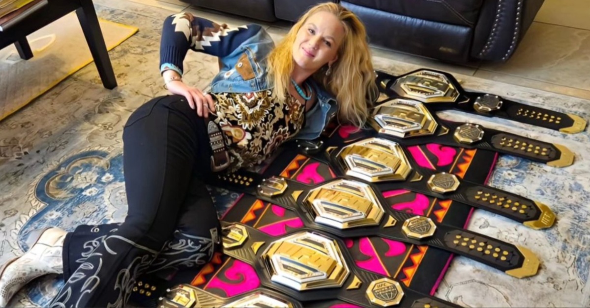 Valentina Shevchenko sits on the floor posing with her seven UFC flyweight title belts