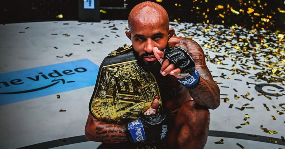 Demetrious Johnson points at the camera while wearing the ONE flyweight championship belt as confetti falls