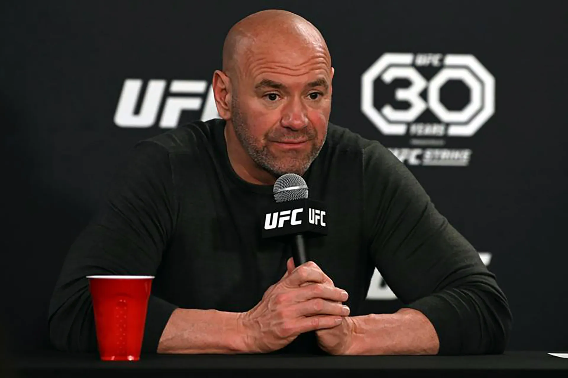 Dana White seated at a UFC post-fight press conference holding a microphone
